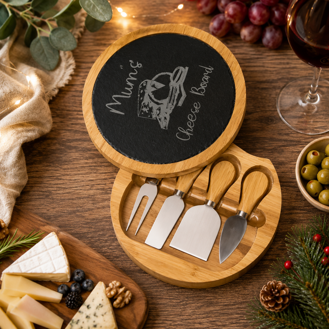 Cheese board set with four tools on a wooden surface with Christmas decorations.