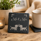 Slate coaster with 'Mr & Mrs' and dog illustrations on a wooden table with a mug and plant.