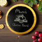 Round cheese board with 'Mum's Cheese Board' text, surrounded by cheese, crackers, and grapes on a wooden surface.