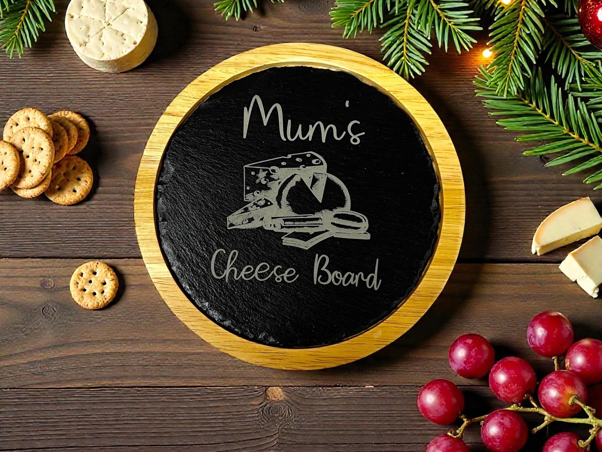 Round cheese board with 'Mum's Cheese Board' text, surrounded by cheese, crackers, and grapes on a wooden surface.
